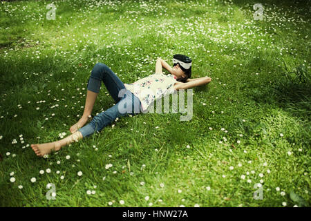 Mixed Race girl laying in grass wearing virtual reality goggles Stock Photo