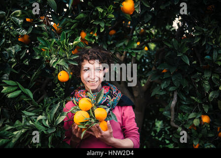 Smiling Caucasian woman holding oranges under tree Stock Photo