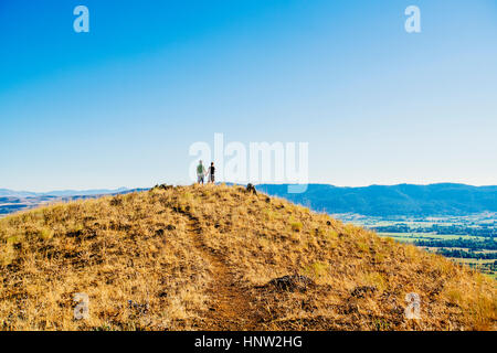 Distant Caucasian couple standing on hill holding hands Stock Photo