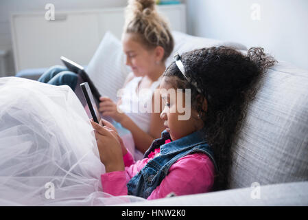 Girls using digital tablets on sofa Stock Photo