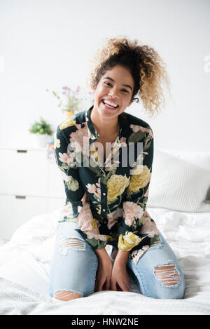 Smiling Mixed Race woman kneeling on bed Stock Photo
