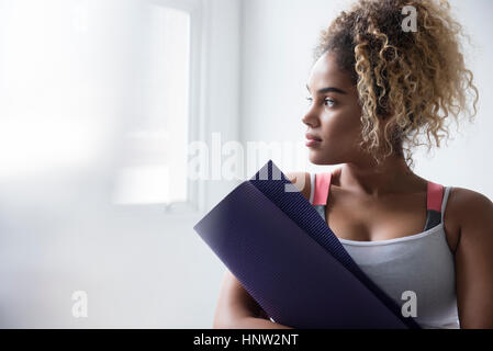 Pensive Mixed Race woman holding rolled up exercise mat Stock Photo