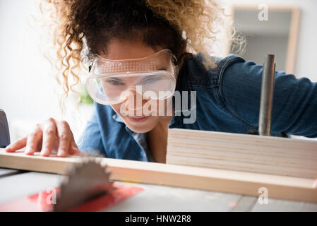 Mixed Race woman cutting wood with saw Stock Photo