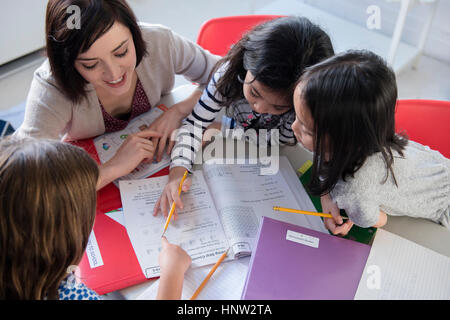 Teacher helping girls with workbook in classroom Stock Photo