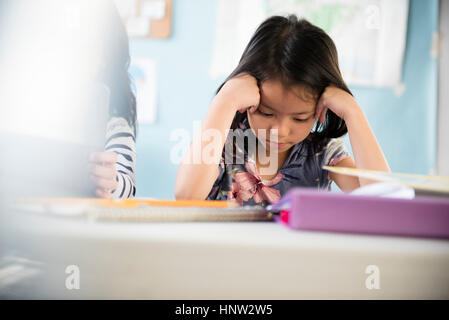 Frustrated girl with head in hands in classroom Stock Photo