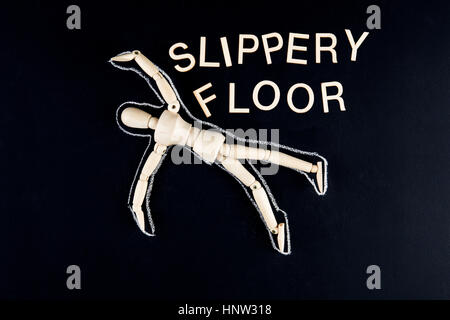 wooden dummy figurine laying on the floor with chalk outline  and 'slippery floor' text Stock Photo