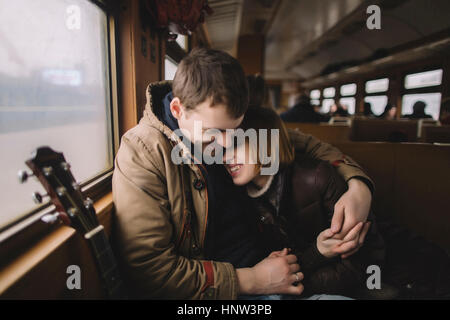 Smiling Caucasian couple with guitar hugging on train Stock Photo
