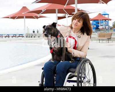 Woman sitting in wheelchair at waterfront with dog in lap Stock Photo