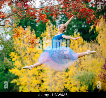 Caucasian ballerina leaping under branches in park Stock Photo