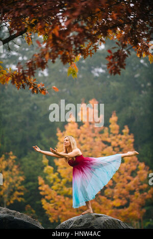Caucasian ballerina dancing on rock in park Stock Photo