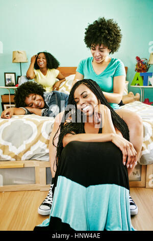 Woman braiding hair of friend in bedroom Stock Photo