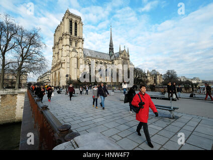A woman in red walking with Notre Dame de Paris; La cathédrale Notre-Dame de Paris in the distance. Stock Photo