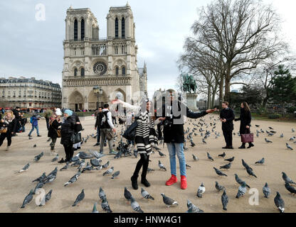 A young couple pose for pictures as they feed pigeons outside the Notre Dame Cathedral in Paris, France Stock Photo