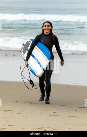 Caucasian woman wearing wetsuit carrying surfboard on beach Stock Photo