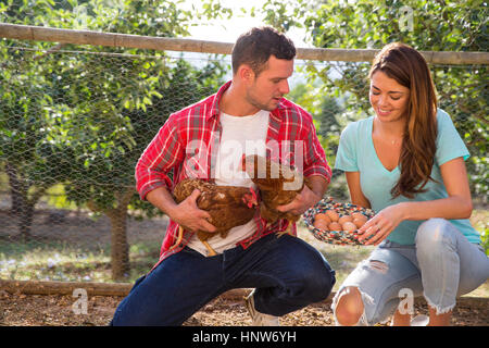 Organic farming couple holding free range chicken and basket of eggs Stock Photo