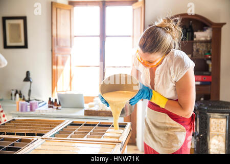 Young woman pouring liquid lavender soap into moulds in handmade soap workshop Stock Photo