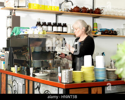 Mature waitress making coffee using coffee machine behind counter Stock Photo