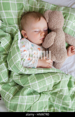 Overhead view of baby boy asleep on bed holding teddy bear Stock Photo