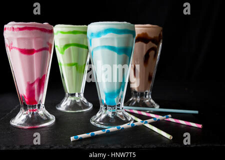 Four colourful milkshakes with drinking straws on table Stock Photo