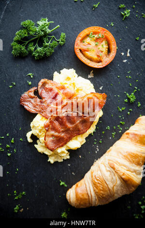 Overhead view of croissant with bacon, omelette and tomato breakfast on slate Stock Photo