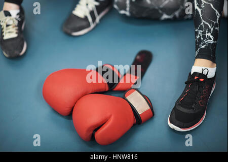 Trainers and feet of female boxers and red boxing gloves  on gym floor Stock Photo