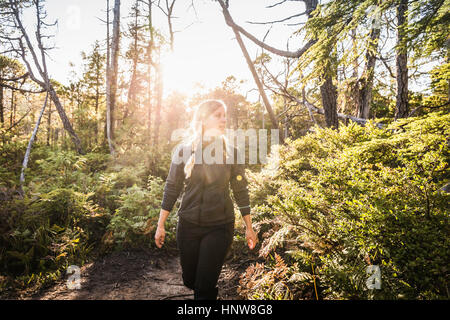 Female hiker hiking through sunlit rainforest, Pacific Rim National Park, Vancouver Island, British Columbia, Canada Stock Photo