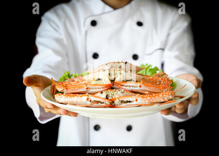 Chef proudly presenting steamed crabs on the plate in dark dramatic background Stock Photo