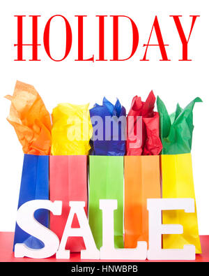 colorful bags with bright tissue paper inserts on a red table with white background and Sale letters. Holiday Sale Stock Photo