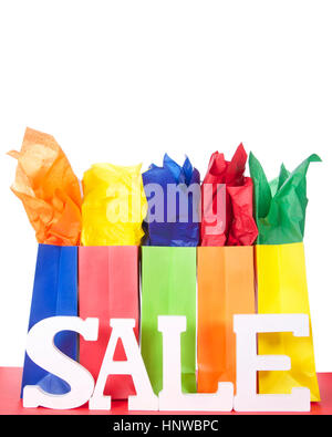 colorful bags with bright tissue paper inserts on a red table with white background and Sale letters. Background blank for your message. Stock Photo