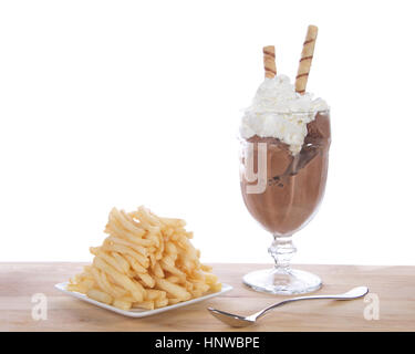 Chocolate ice cream in glass cup with whipped cream and square white plate of stacked french fries on a light wood table. Food fad or new trend. Stock Photo