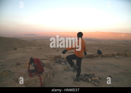 A 61 year old senior citizen hiker is holding her balance while standing n a small rock exercising at sunrise. Makhtesh Ramon, Negev Desert, Israel. Stock Photo