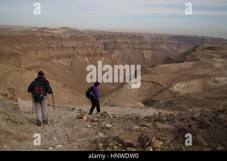 Two women hikers hike on a marked trek and start descending the steep walls of the deep canyon of Nahal Tzeelim, the Judean Desert, Israel. Stock Photo
