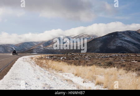 Rear view of recreational vehicle driving on snowy rural road toward mountains, Idaho Stock Photo