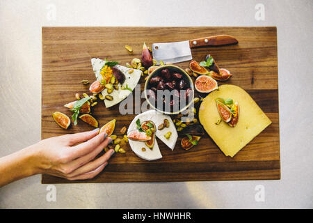 Variety cheese plate with figs, olives, pistachios, cleaver on wooden chopping board Stock Photo