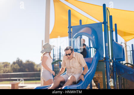 Family at playground, father sliding down slide Stock Photo