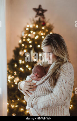 Mid adult woman cradling new born baby daughter wrapped in cardigan at Christmas Stock Photo