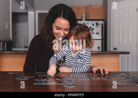 Girl at table doing jigsaw puzzle with mother Stock Photo