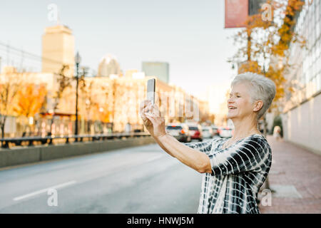Senior woman outdoors, using smartphone, smiling Stock Photo
