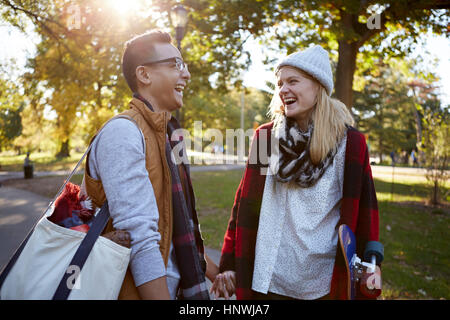 Young female skateboarder laughing with boyfriend in park Stock Photo