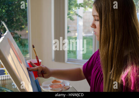 Teenage female artist painting on canvas in conservatory