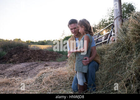 Father and daughter standing together on farm, daughter holding hay Stock Photo