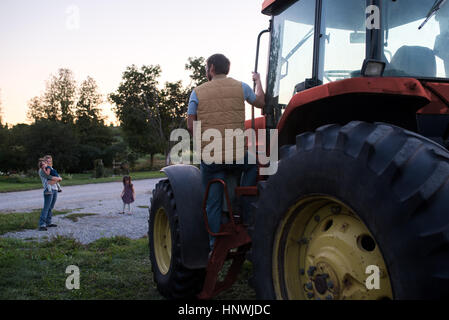 Family on farm, father climbing into tractor Stock Photo