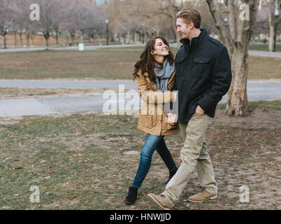 Young couple walking through park, arm in arm, smiling Stock Photo