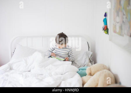 Boy sitting up in bed playing video game on digital tablet Stock Photo