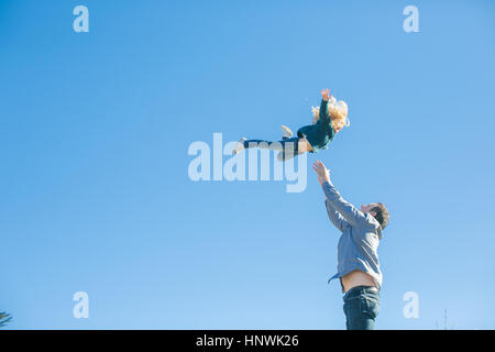 Girl being thrown mid air by father against blue sky Stock Photo