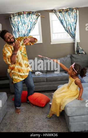 Girl in fairy costume casting spell on father in living room Stock Photo