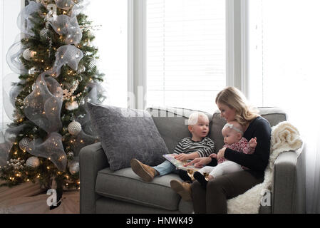 Mother and children sitting on sofa, looking at book Stock Photo