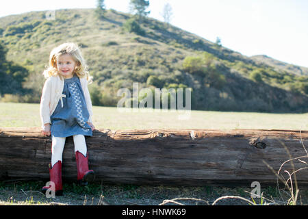 Portrait of girl sitting on log wearing red cowboy boots Stock Photo