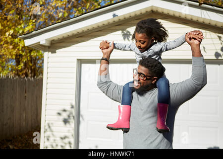 Mature man carrying daughter on shoulders by residential garage Stock Photo