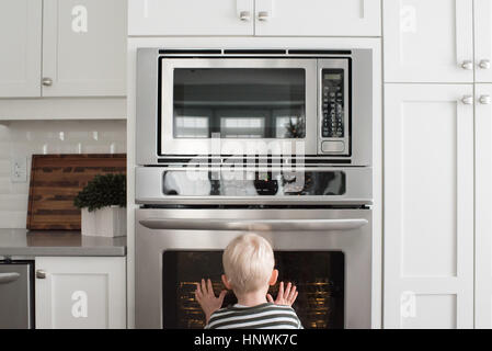 Young boy in kitchen looking through oven door Stock Photo